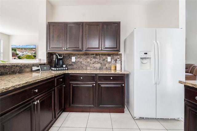 kitchen with white fridge with ice dispenser, dark brown cabinets, backsplash, and light stone countertops