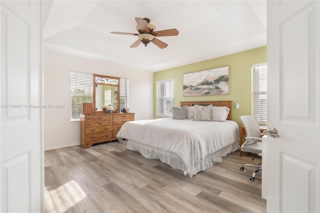 bedroom with a tray ceiling, light wood-type flooring, a ceiling fan, and baseboards