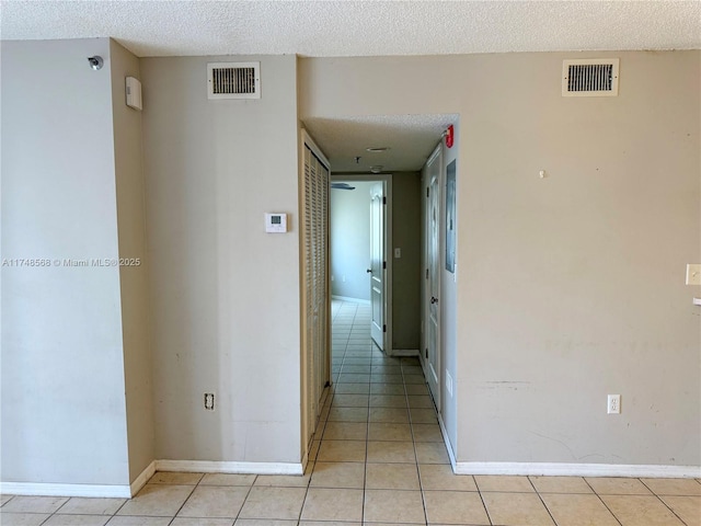 hallway with visible vents, a textured ceiling, and light tile patterned flooring