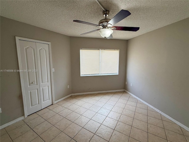 unfurnished bedroom featuring light tile patterned floors, a closet, a textured ceiling, and baseboards