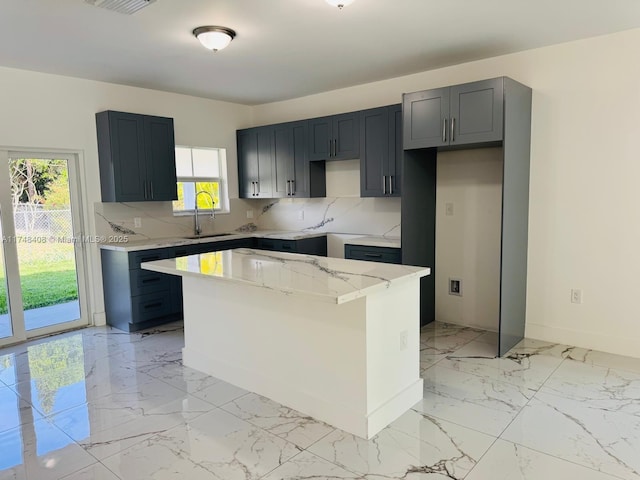 kitchen with decorative backsplash, marble finish floor, a kitchen island, and a sink