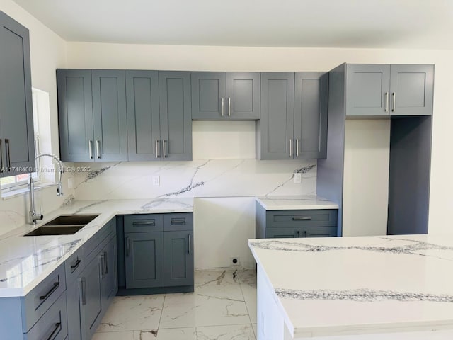 kitchen featuring tasteful backsplash, marble finish floor, a sink, and light stone countertops