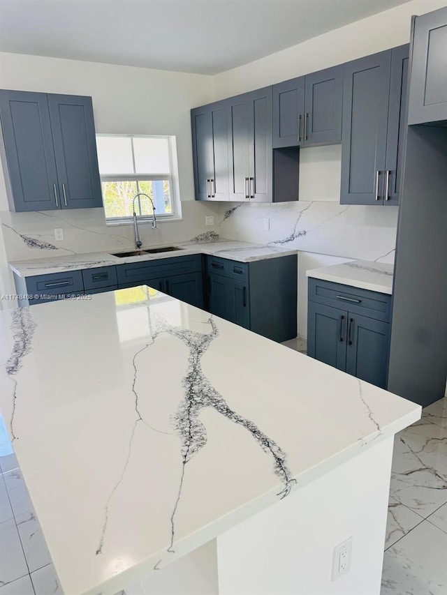 kitchen with marble finish floor, tasteful backsplash, a sink, and light stone countertops