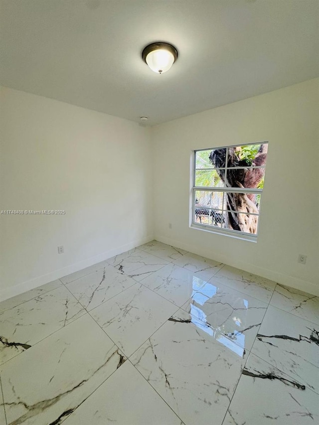 unfurnished room featuring marble finish floor and baseboards