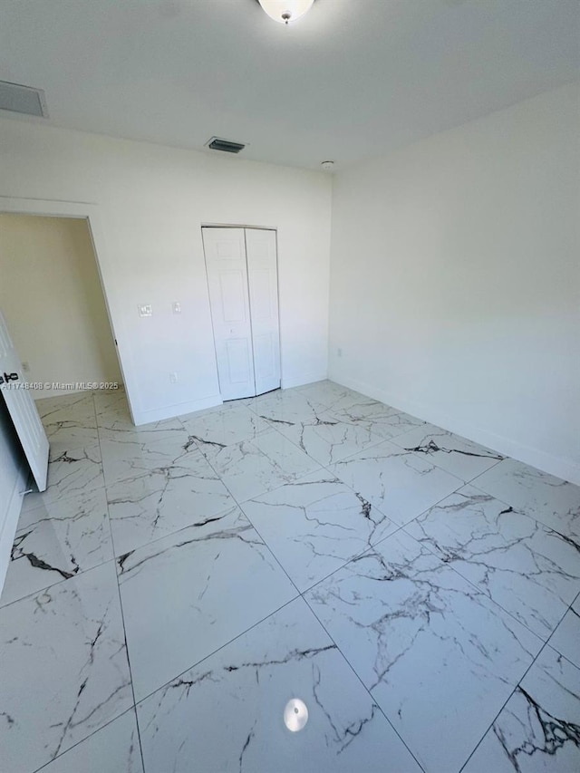 unfurnished bedroom featuring marble finish floor, baseboards, visible vents, and a closet