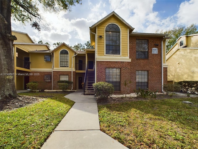 exterior space featuring brick siding, stairway, and a front lawn