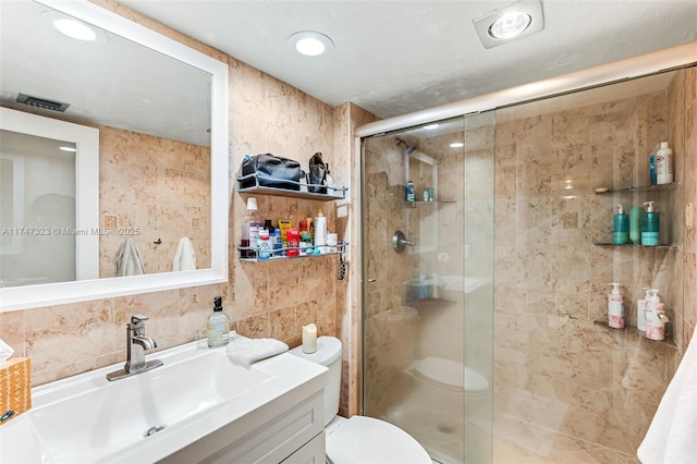 bathroom featuring visible vents, toilet, vanity, a shower stall, and tile walls