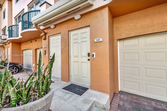 view of exterior entry featuring a garage, a balcony, and stucco siding