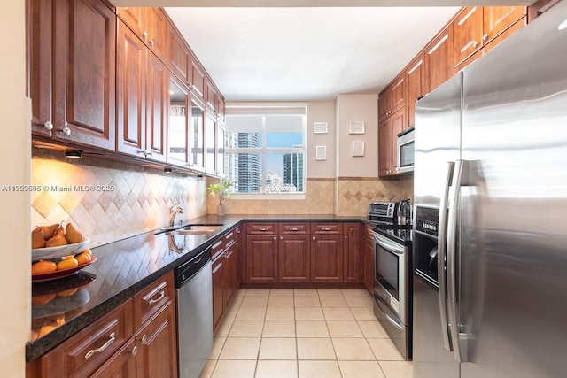 kitchen featuring light tile patterned flooring, a sink, appliances with stainless steel finishes, tasteful backsplash, and dark stone countertops