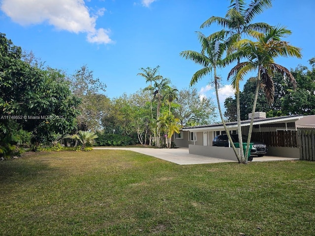 view of yard featuring a carport, concrete driveway, a patio area, and fence