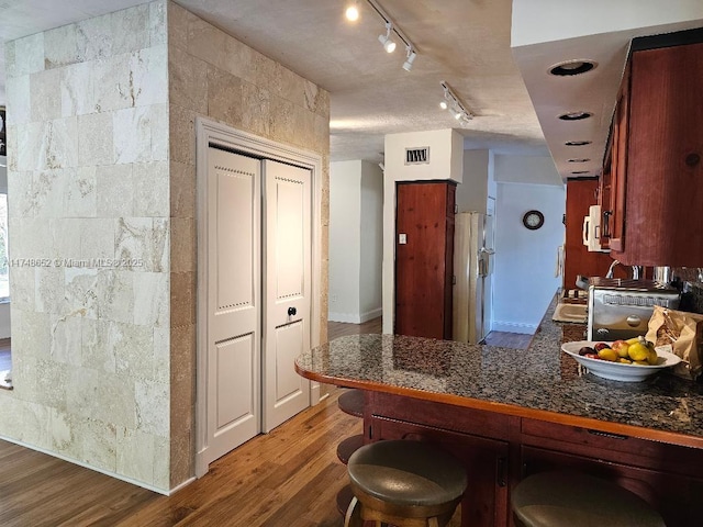 kitchen featuring visible vents, dark countertops, wood finished floors, a peninsula, and a kitchen bar