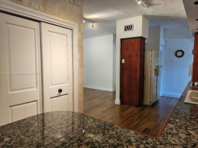 interior space featuring a textured ceiling, white refrigerator with ice dispenser, dark wood-type flooring, visible vents, and tile counters