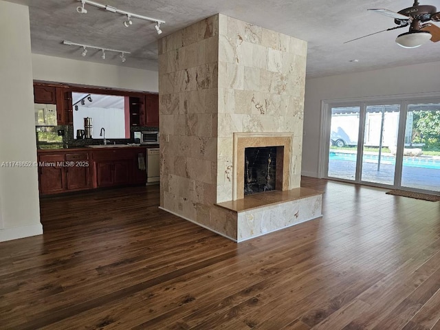 unfurnished living room featuring a tile fireplace, dark wood finished floors, a sink, and ceiling fan