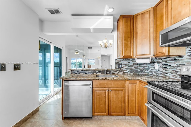 kitchen featuring visible vents, decorative light fixtures, light stone countertops, stainless steel appliances, and a sink