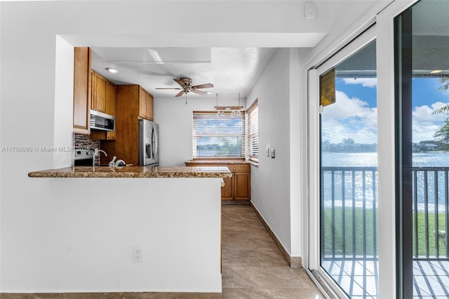 kitchen featuring stainless steel appliances, brown cabinetry, a water view, and a peninsula