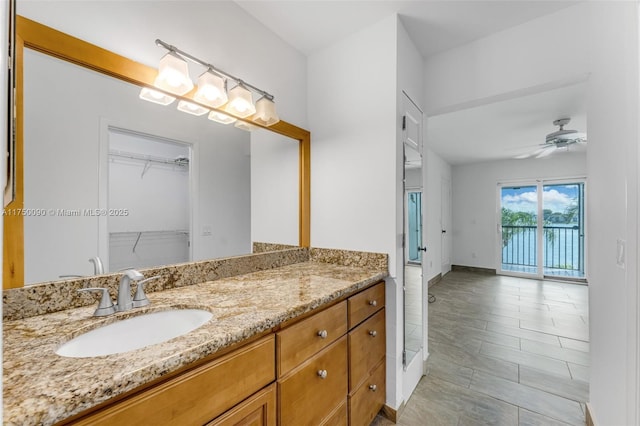 bathroom featuring a walk in closet, ceiling fan, vanity, and baseboards