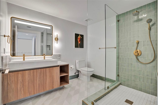 bathroom featuring visible vents, toilet, vanity, a walk in shower, and baseboards