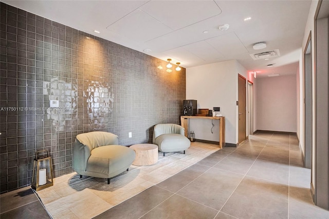 sitting room with baseboards, light tile patterned flooring, visible vents, and tile walls