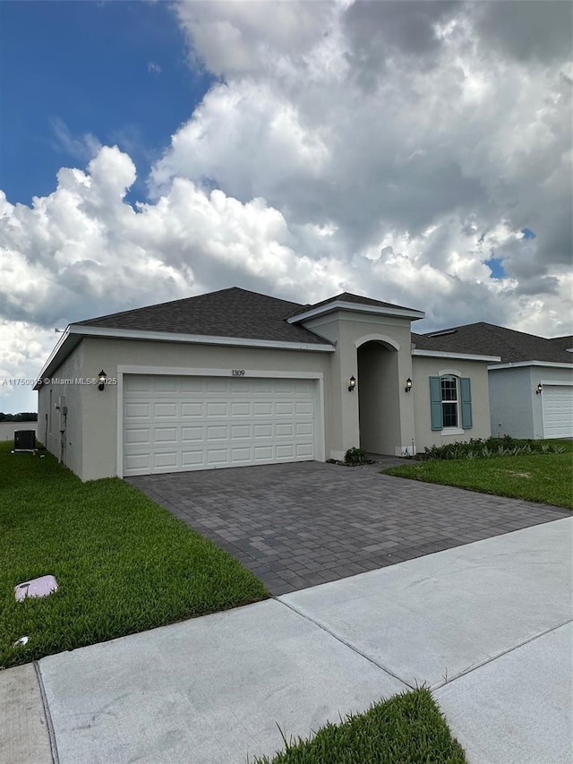 ranch-style house with a front yard, decorative driveway, an attached garage, and stucco siding