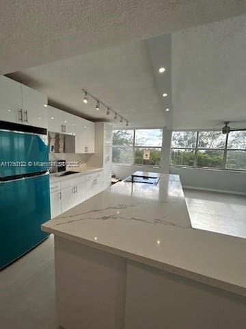 kitchen with freestanding refrigerator, white cabinets, a textured ceiling, light stone countertops, and stovetop