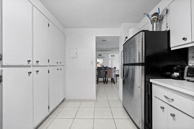 kitchen with light tile patterned floors, baseboards, freestanding refrigerator, light countertops, and white cabinets