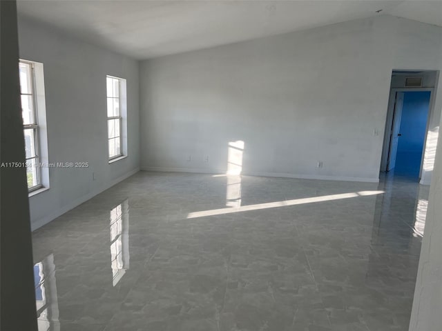 empty room featuring marble finish floor, baseboards, and vaulted ceiling