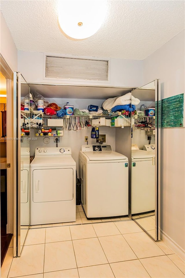 washroom featuring laundry area, washer and clothes dryer, a textured ceiling, and light tile patterned floors