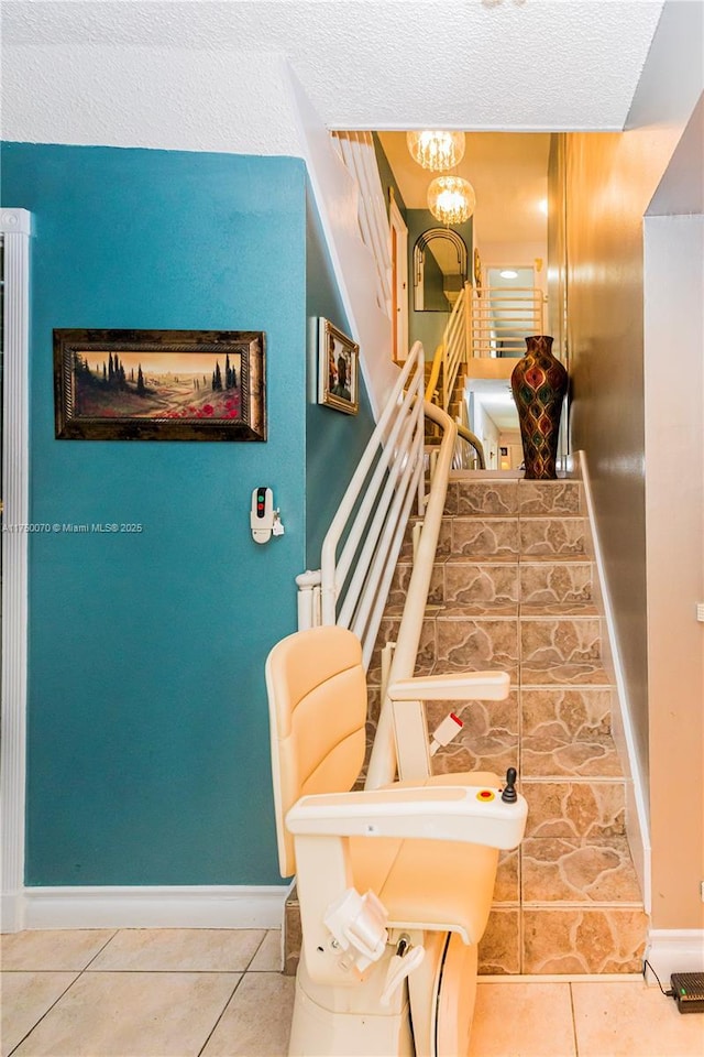 staircase with tile patterned flooring, a notable chandelier, and baseboards