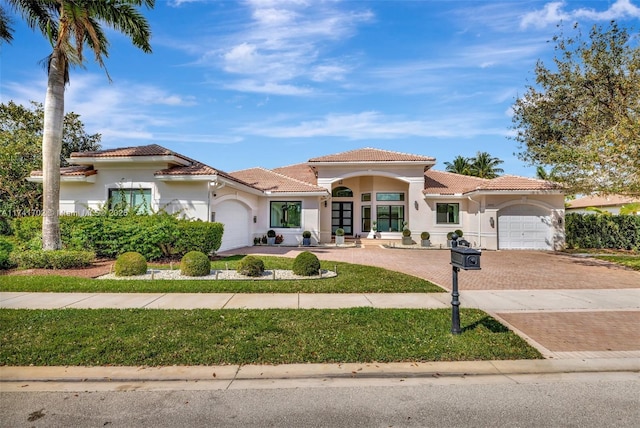 mediterranean / spanish-style home with decorative driveway, a tile roof, an attached garage, and stucco siding