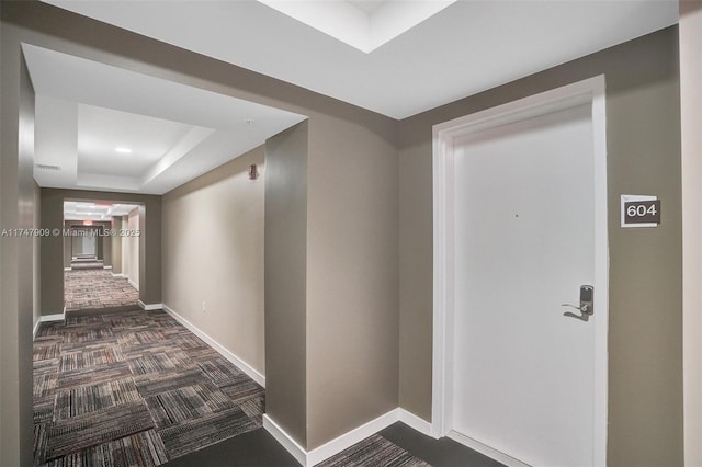 corridor with visible vents, baseboards, dark colored carpet, and a raised ceiling