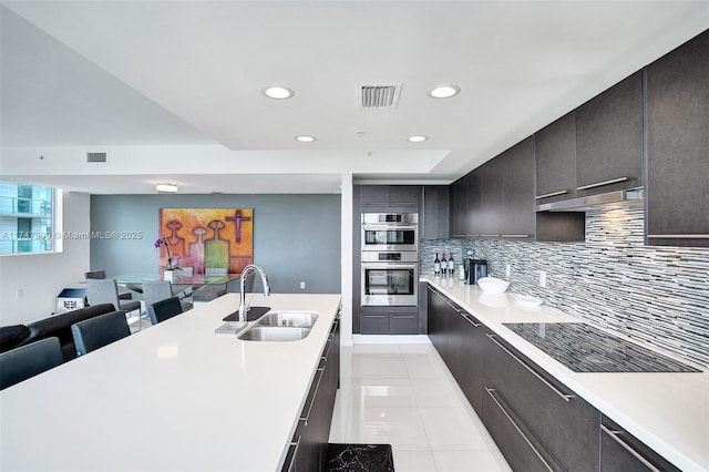 kitchen featuring visible vents, stainless steel double oven, a sink, decorative backsplash, and light countertops