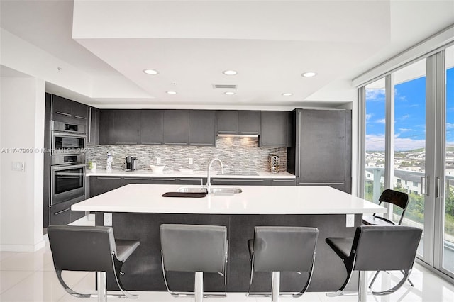 kitchen featuring visible vents, a breakfast bar, a sink, light countertops, and decorative backsplash