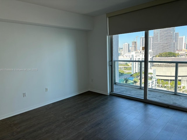 unfurnished room featuring dark wood-style floors, baseboards, a wealth of natural light, and a city view