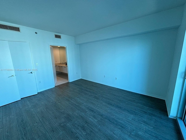 unfurnished bedroom featuring ensuite bath, baseboards, visible vents, and dark wood-type flooring