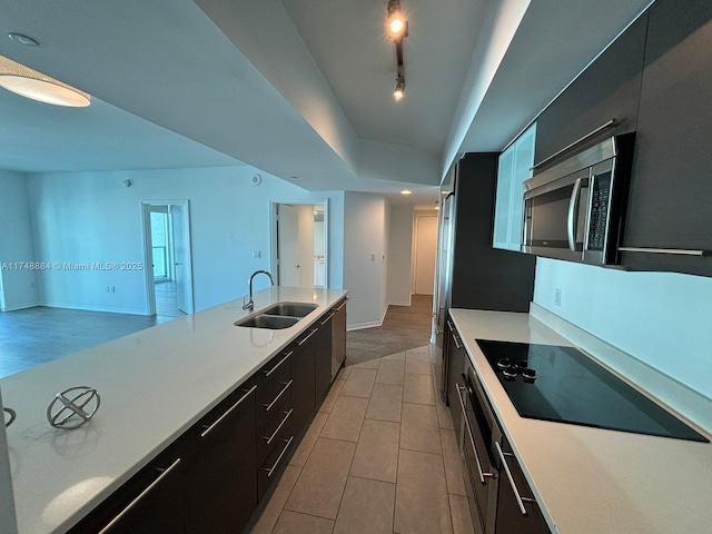 kitchen with light countertops, stainless steel microwave, a sink, track lighting, and modern cabinets