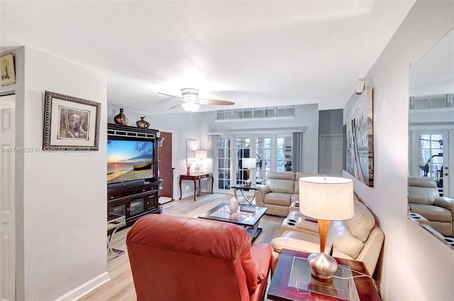 living area with light wood-style floors, ceiling fan, baseboards, and french doors