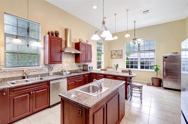 kitchen with stainless steel appliances, a center island with sink, a sink, and wall chimney exhaust hood