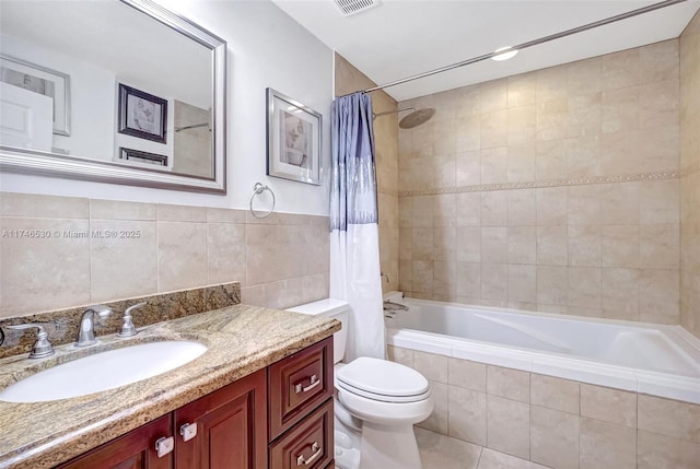 bathroom featuring visible vents, toilet, tiled shower / bath, vanity, and tile walls