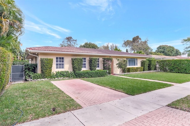 ranch-style home with a tiled roof, a front yard, fence, and stucco siding