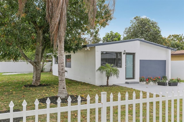 view of front facade with a garage, a fenced front yard, a front lawn, and stucco siding