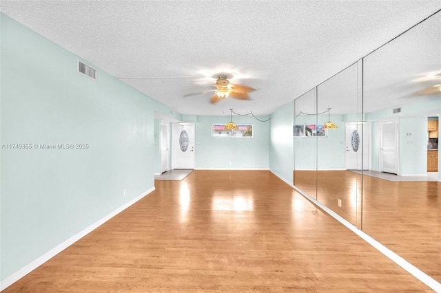 interior space featuring visible vents, ceiling fan, a textured ceiling, and wood finished floors