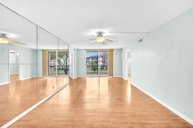 spare room with baseboards, light wood-type flooring, a ceiling fan, and floor to ceiling windows