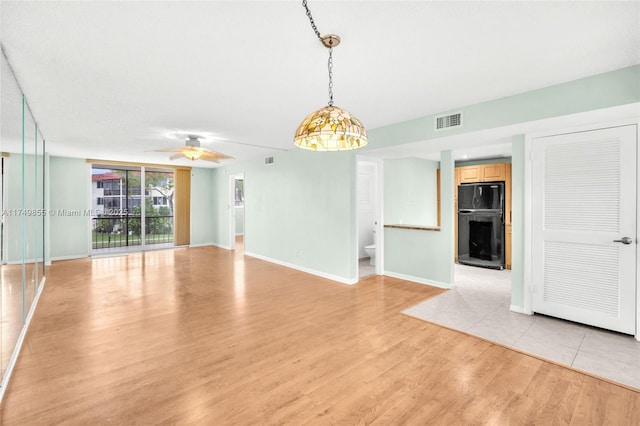 spare room featuring a fireplace, a ceiling fan, visible vents, baseboards, and light wood finished floors