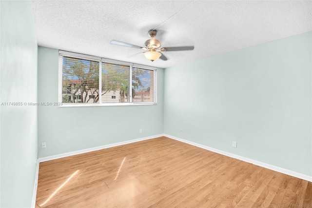 empty room with a textured ceiling, wood finished floors, a ceiling fan, and baseboards