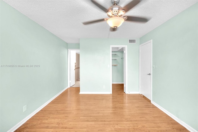 unfurnished bedroom with a textured ceiling, visible vents, baseboards, a spacious closet, and light wood-type flooring