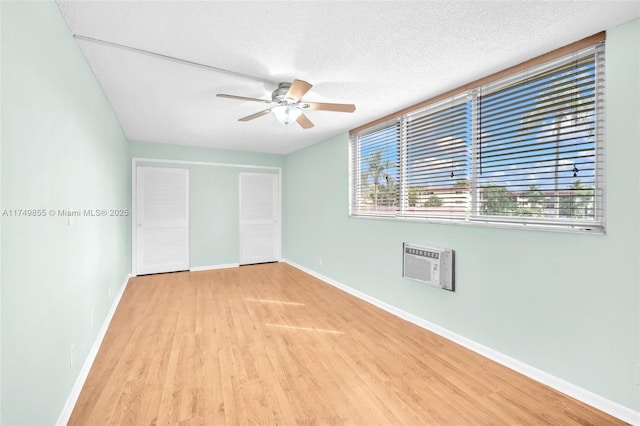 unfurnished bedroom featuring a textured ceiling, light wood finished floors, a wall mounted AC, and baseboards