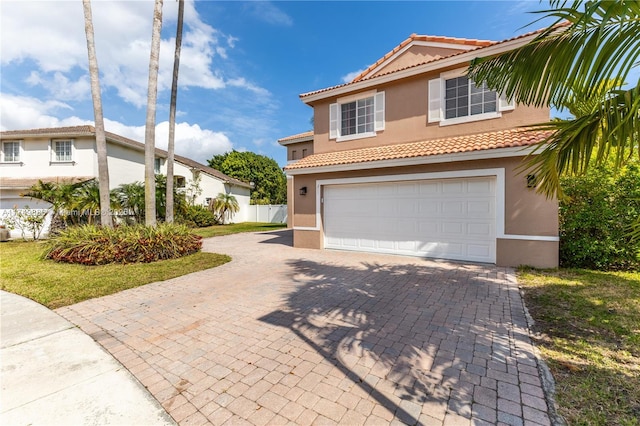 mediterranean / spanish-style house with a garage, decorative driveway, fence, and stucco siding