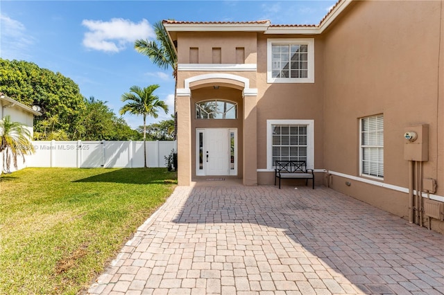 entrance to property featuring a lawn, a patio, a tile roof, fence, and stucco siding