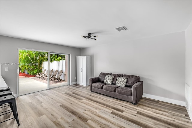 living room with light wood-type flooring, visible vents, and baseboards