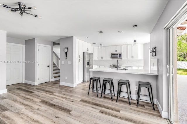 kitchen with a peninsula, stainless steel appliances, white cabinetry, light wood-style floors, and light countertops